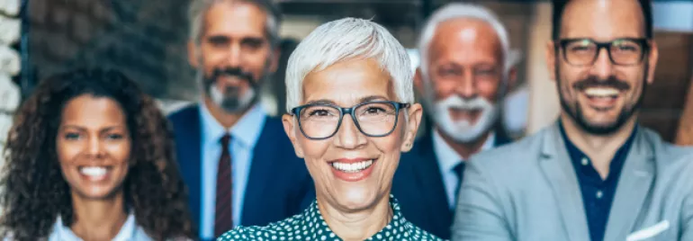 Smiling team of diverse professionals with a woman in glasses at the front.